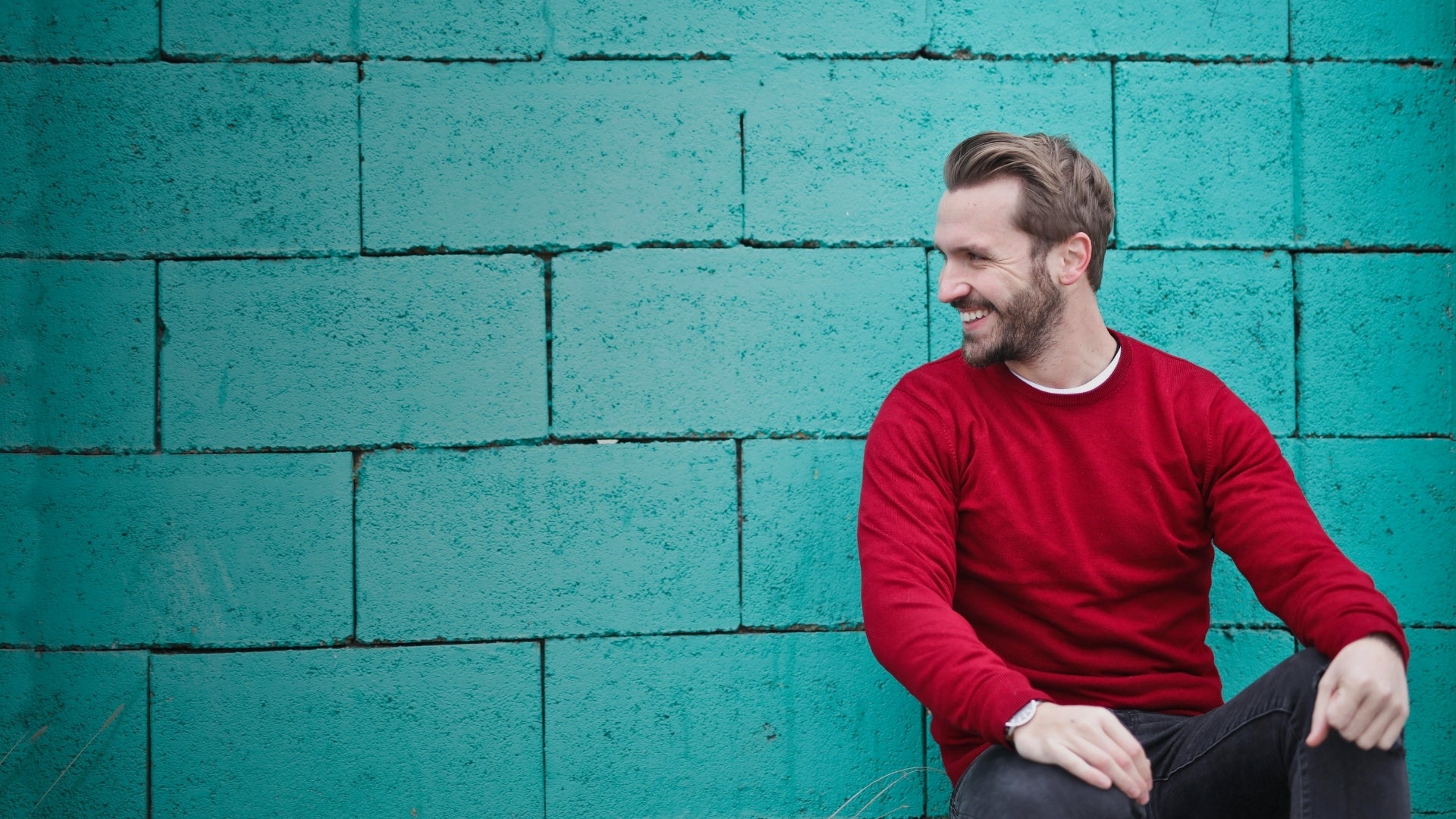Smiling man in bright red crew neck sweater against turquoise wall